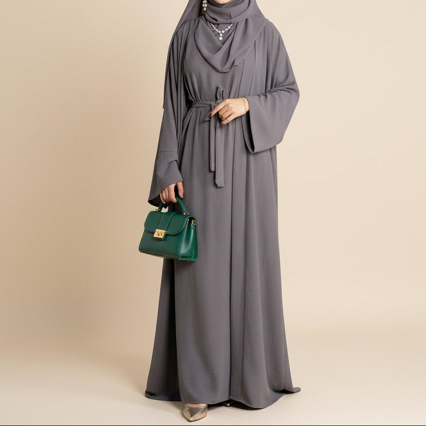 Woman wearing a gray abaya with a green handbag on a beige background
