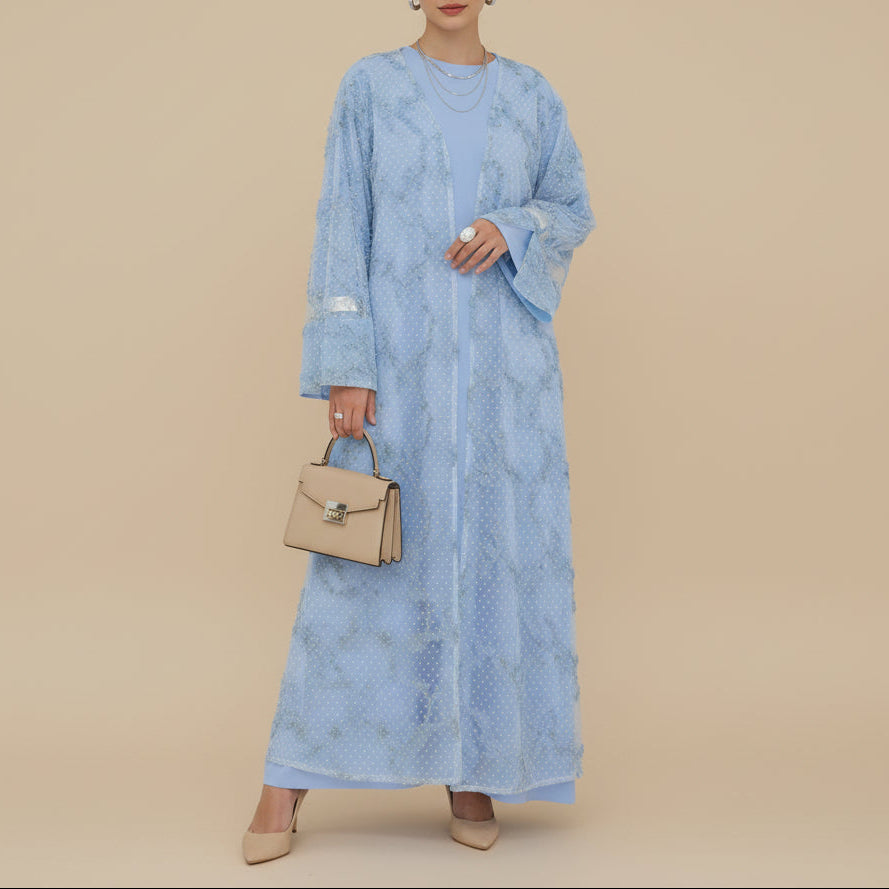 Woman wearing a blue dress holding a beige handbag against a beige background