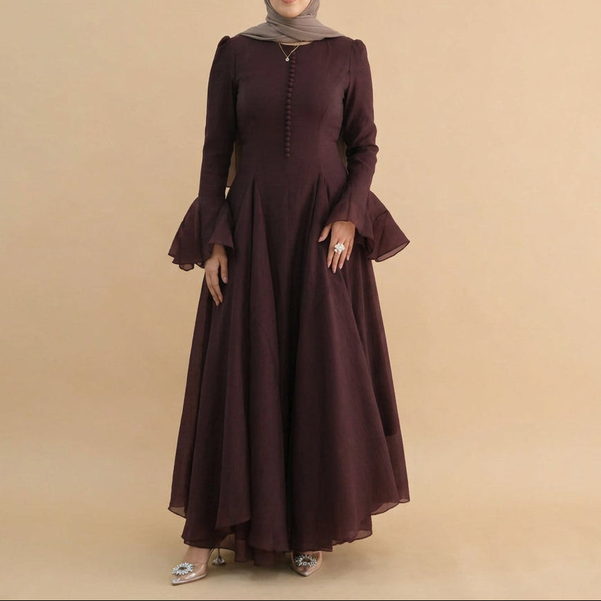 A woman modeling a long-sleeved, floor-length maroon dress with a buttoned neckline and flared bell sleeves, set against a plain white studio background.