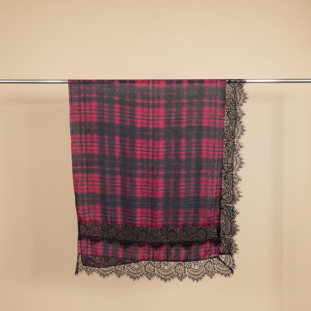 A square scarf with a vibrant pink and dark gray plaid pattern, finished with a black lace border, hanging from a metal rod against a plain white wall.