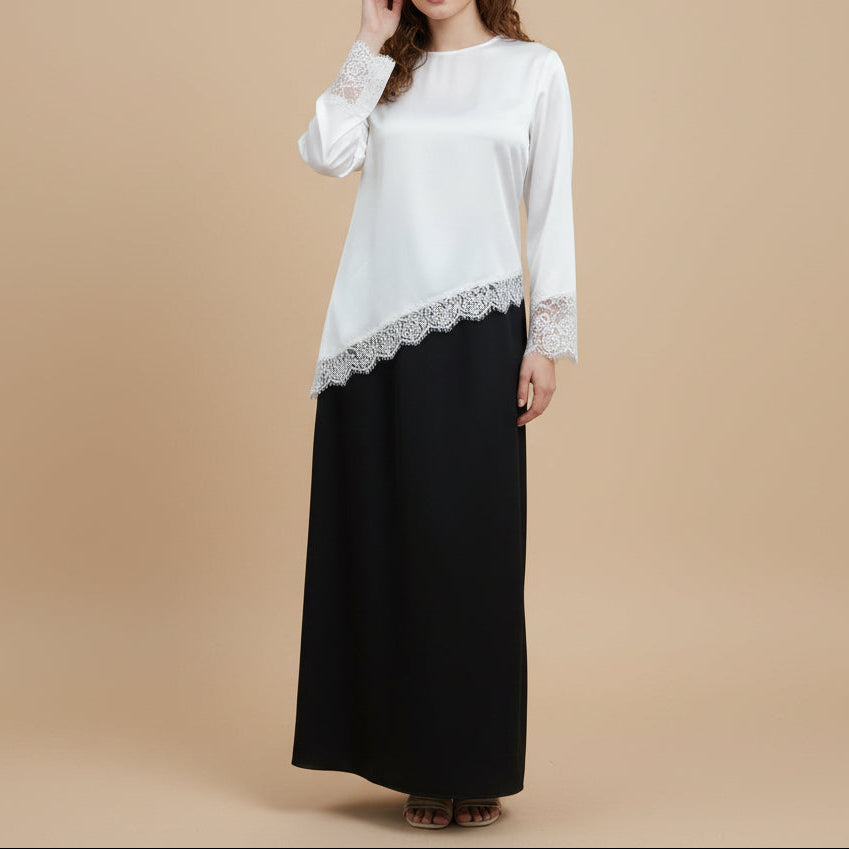 Woman wearing a white top with lace details and a black skirt in a minimalistic room.