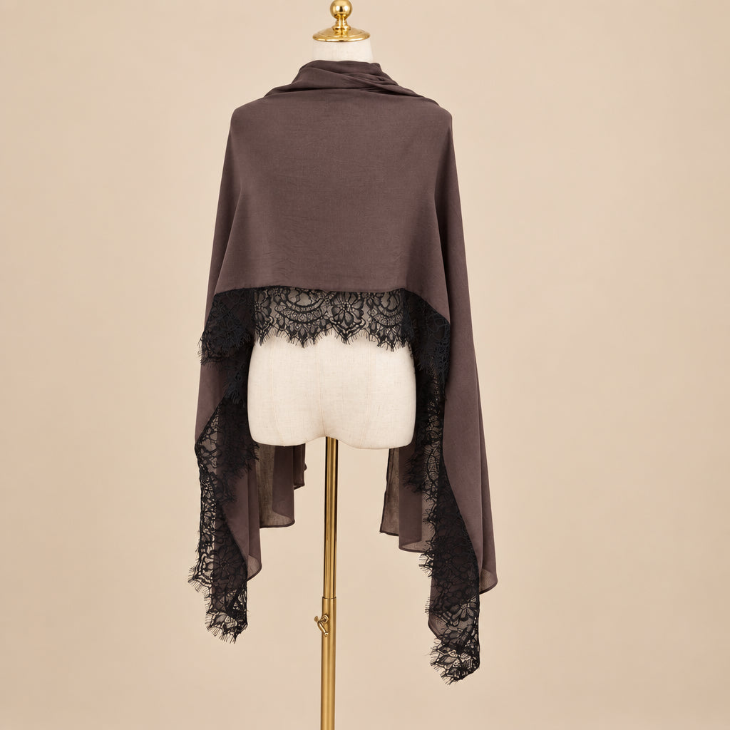 A brown shawl with black lace trim draped over a cream-colored mannequin torso, set against a beige background 
