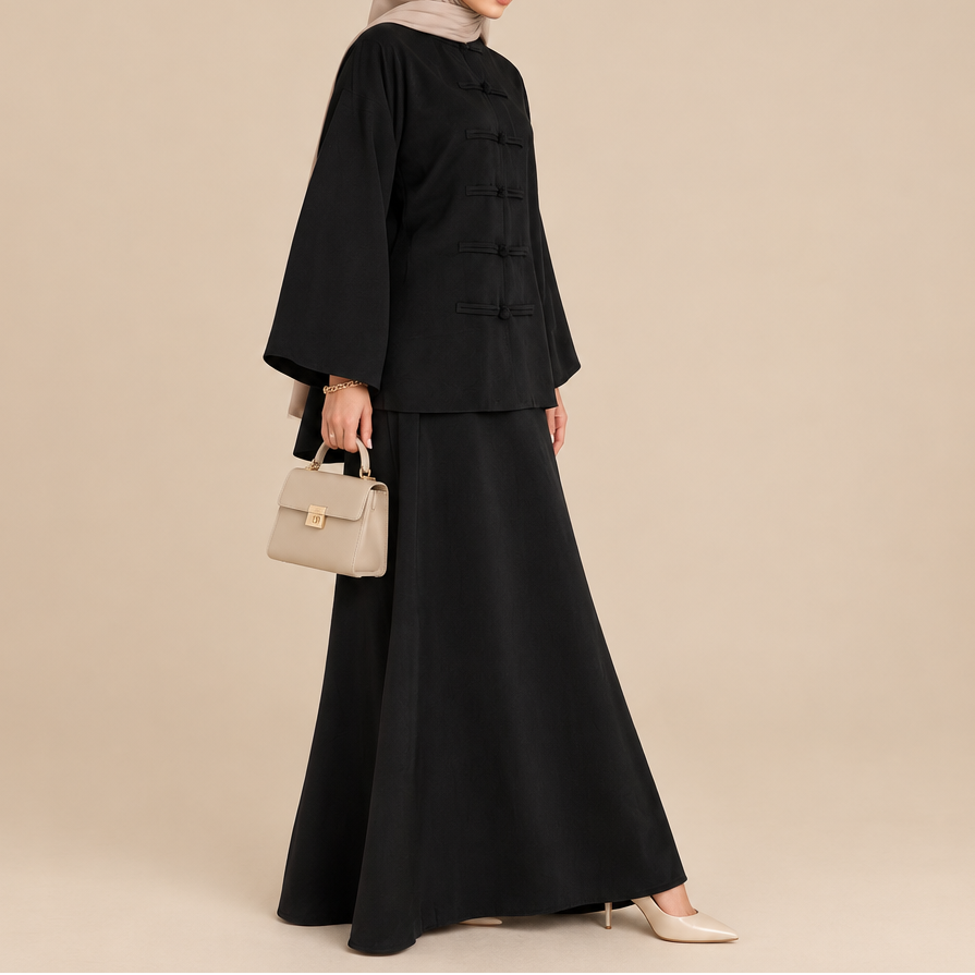 A woman wearing a black long-sleeve modest outfit with a matching skirt and a beige hijab stands on a cafe patio. She is carrying a tan shoulder bag and wearing beige slip-on shoes.