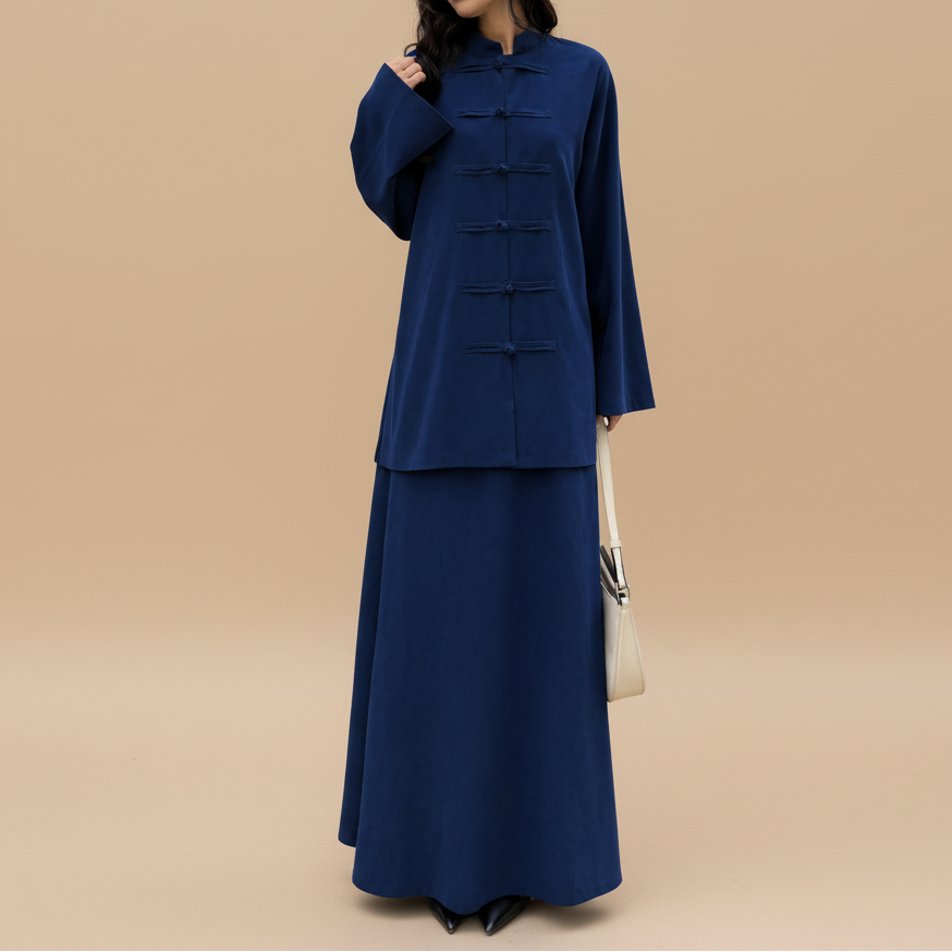A woman wearing a dark blue traditional Chinese-style long dress with frog closures stands in front of a storefront with glass doors.