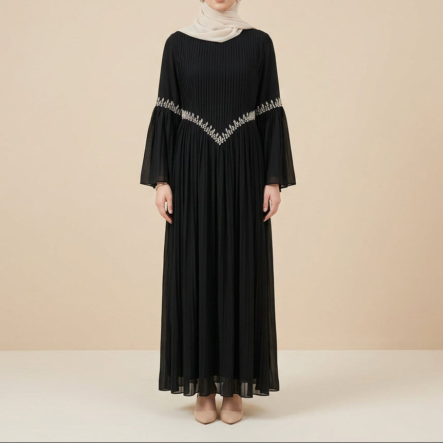 A black long-sleeve maxi dress with a pleated skirt and a decorative silver geometric pattern across the upper chest and shoulders, displayed on a mannequin against a white paneled wall.