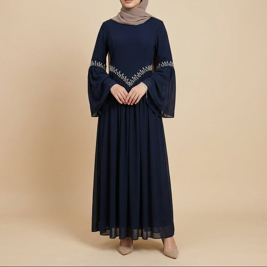 A long navy blue maxi dress displayed on a mannequin against a white paneled wall. The dress has three-quarter bell sleeves with decorative silver beaded trim along the arm openings and a matching beaded V-shaped detail across the chest.