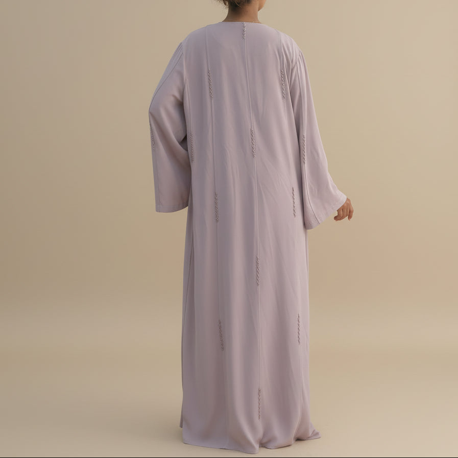 Person wearing a long light pink abaya dress against a beige background