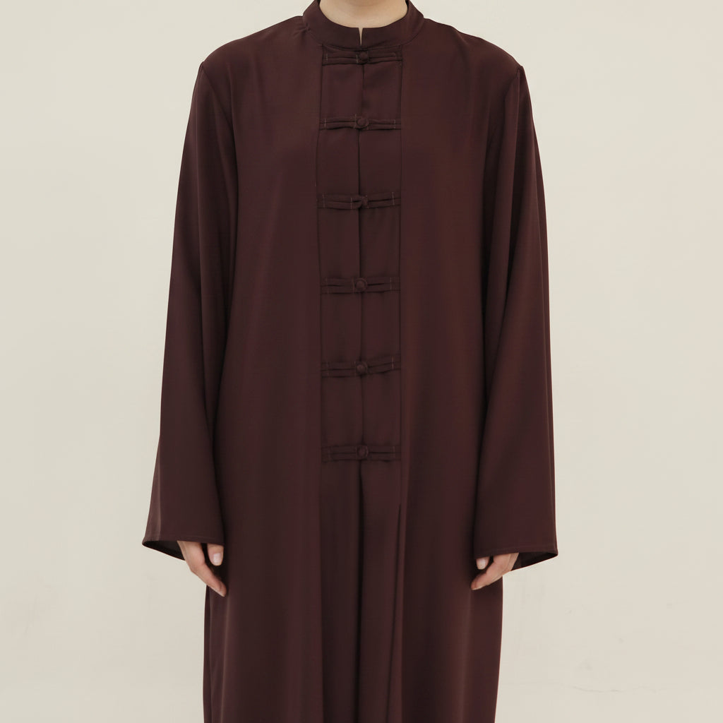 A dark brown long-sleeve tunic with a high mock neck and traditional Chinese-style frog closures down the front, shown on a model against a plain white background.
