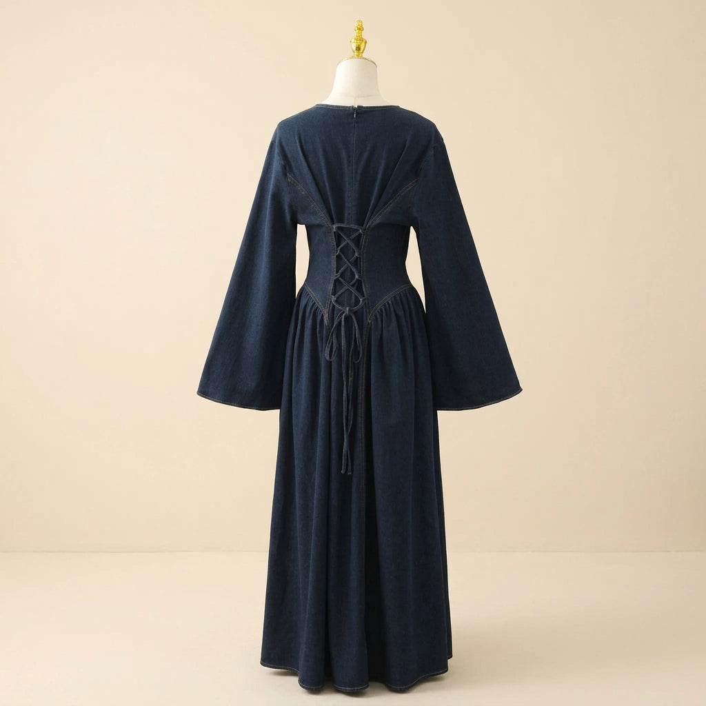 A dark blue denim long-sleeve dress displayed on a cream dress form against a white paneled wall. The back of the dress features a lace-up corset-style waist with matching dark blue laces.