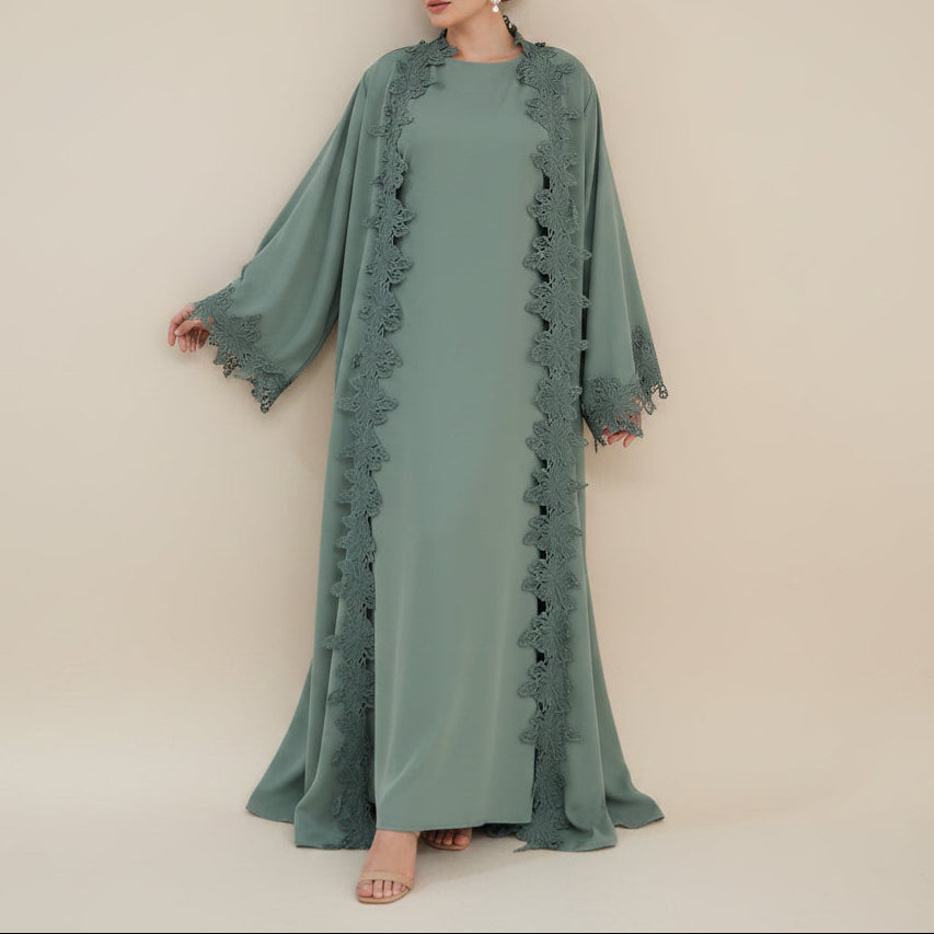 A woman modeling a long sage green abaya dress with matching long sleeves and scalloped lace trim along the front opening, shown against a plain beige studio background.