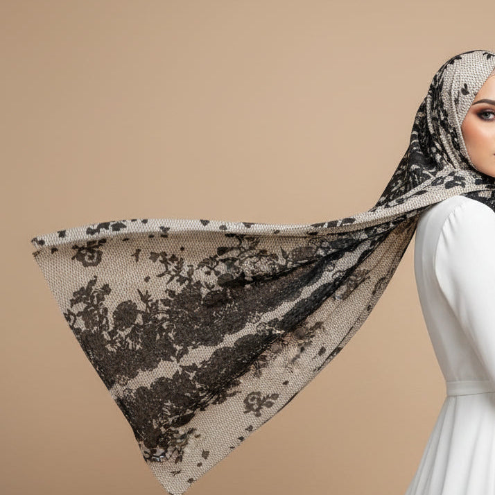 Woman wearing a long white dress and a premium Midnight Chantilly lace print modal hijab sweeping dynamically in the wind against a beige studio backdrop.