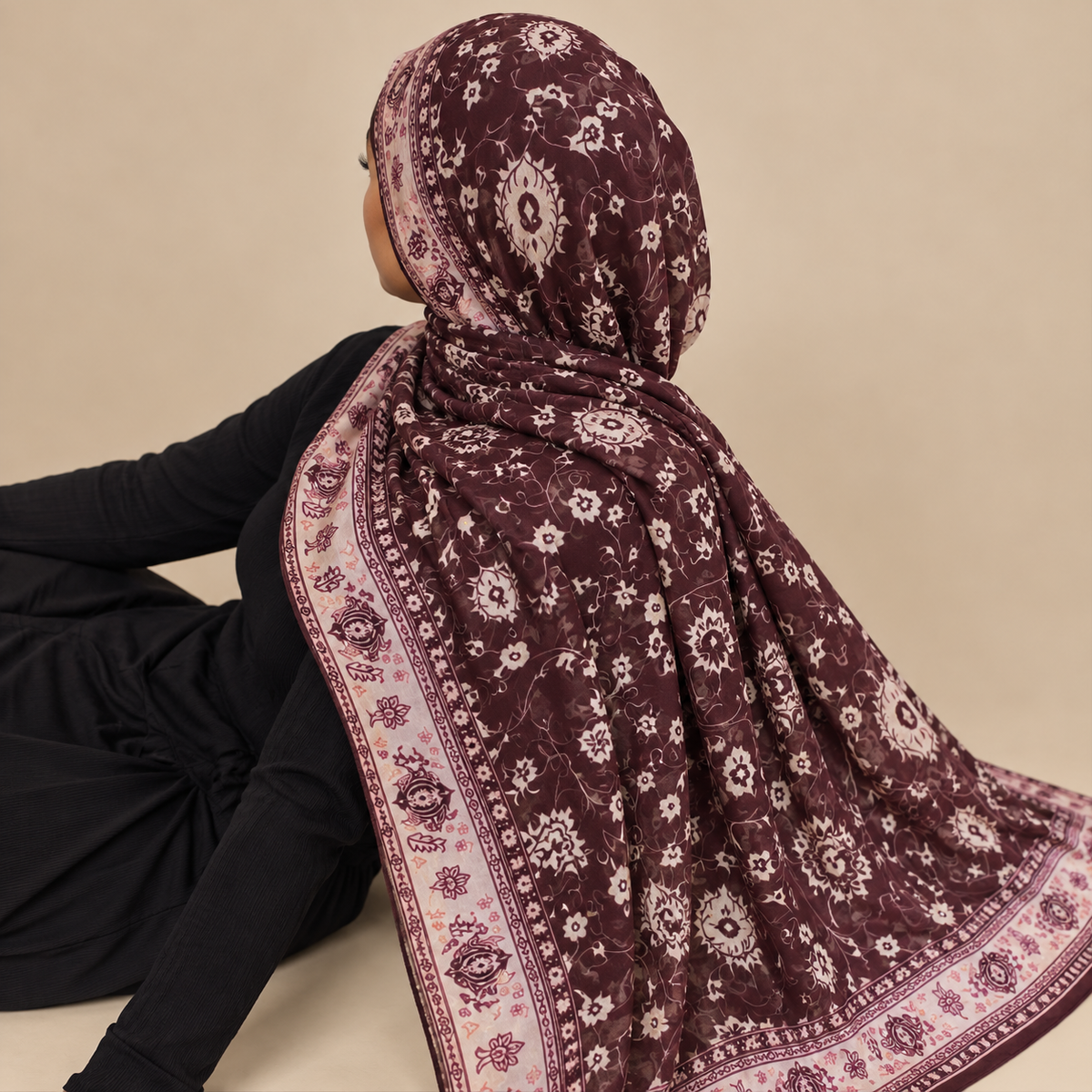 A woman wearing a dark plum purple and pink floral patterned modal hijab, shown from the back and side against a solid beige background.