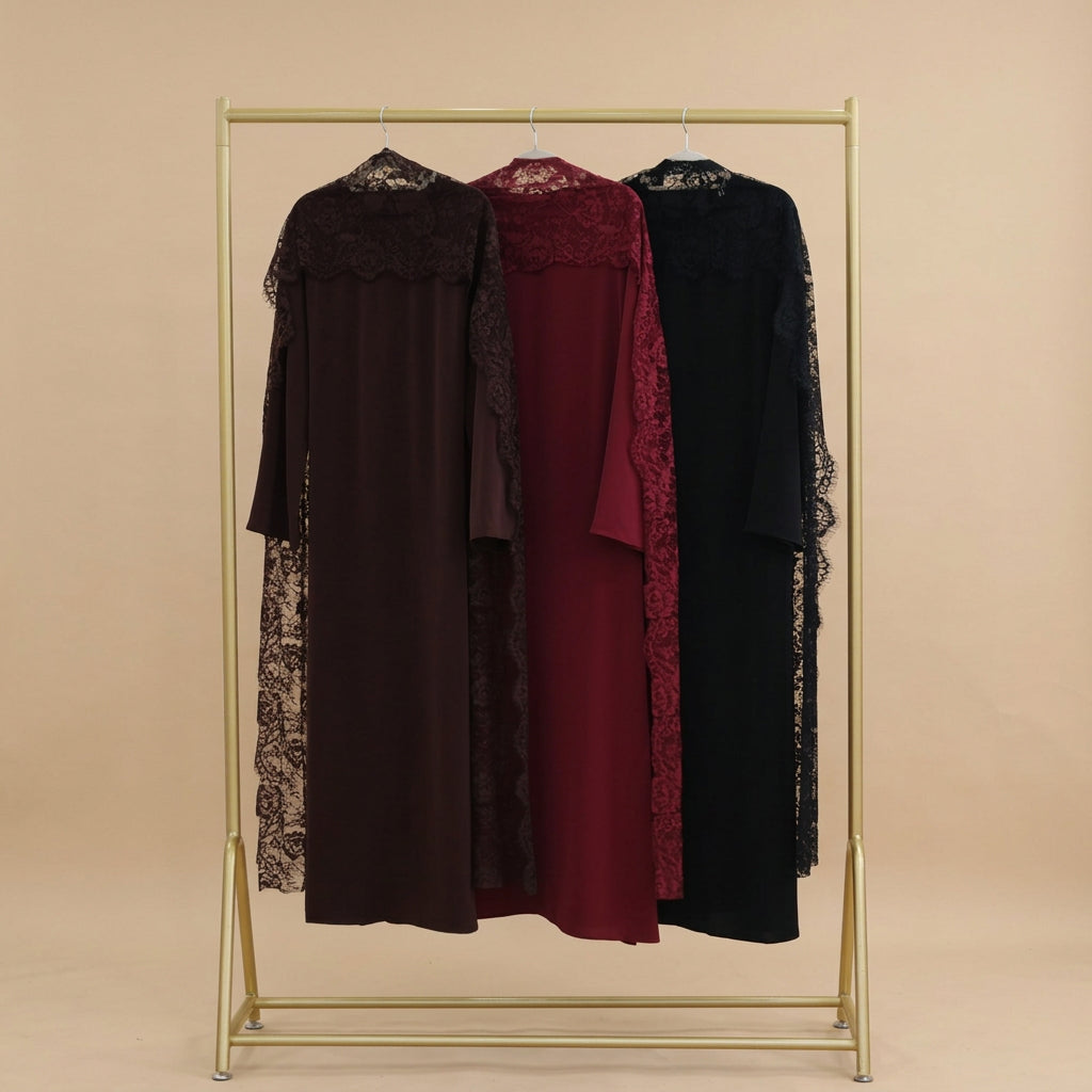 Three long lace-trimmed kaftan-style dresses in dark brown, deep red, and black hang on a gold metal clothing rack against a white paneled wall.