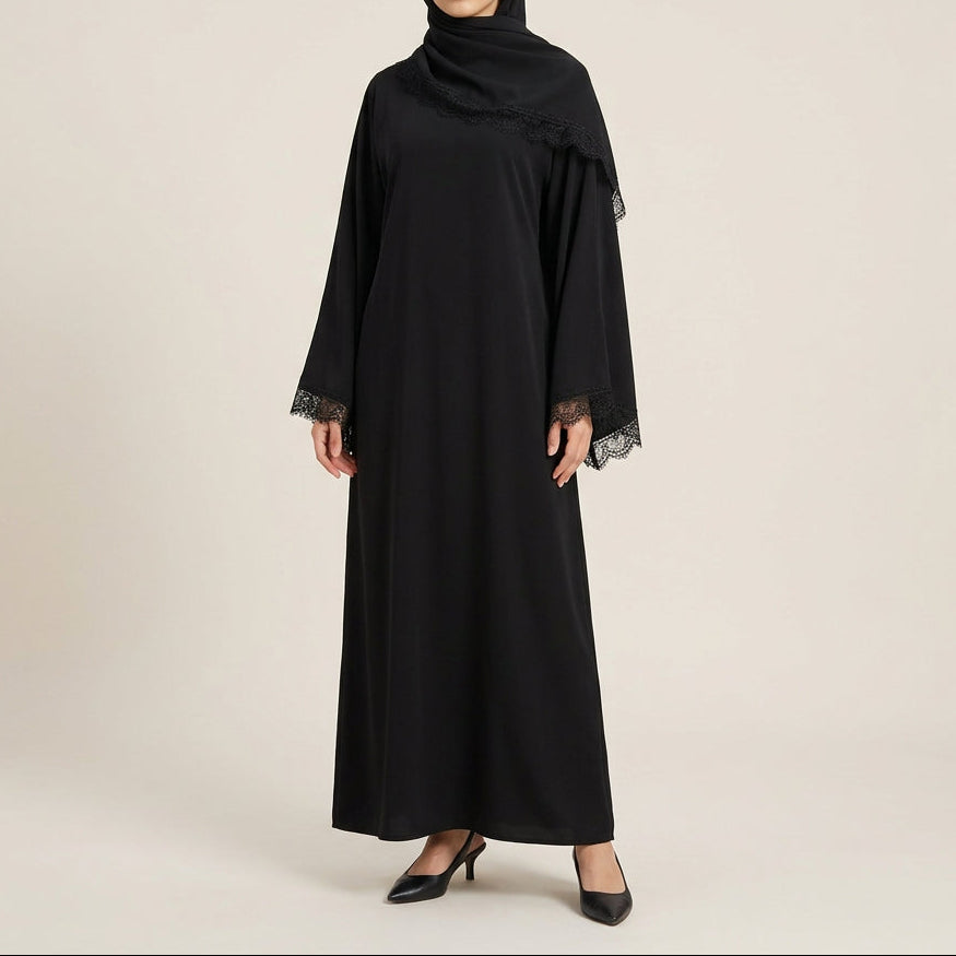 A black long-sleeve abaya dress displayed on a mannequin, featuring sheer lace trim at the cuffs and a matching draped shawl, set against a white paneled wall.