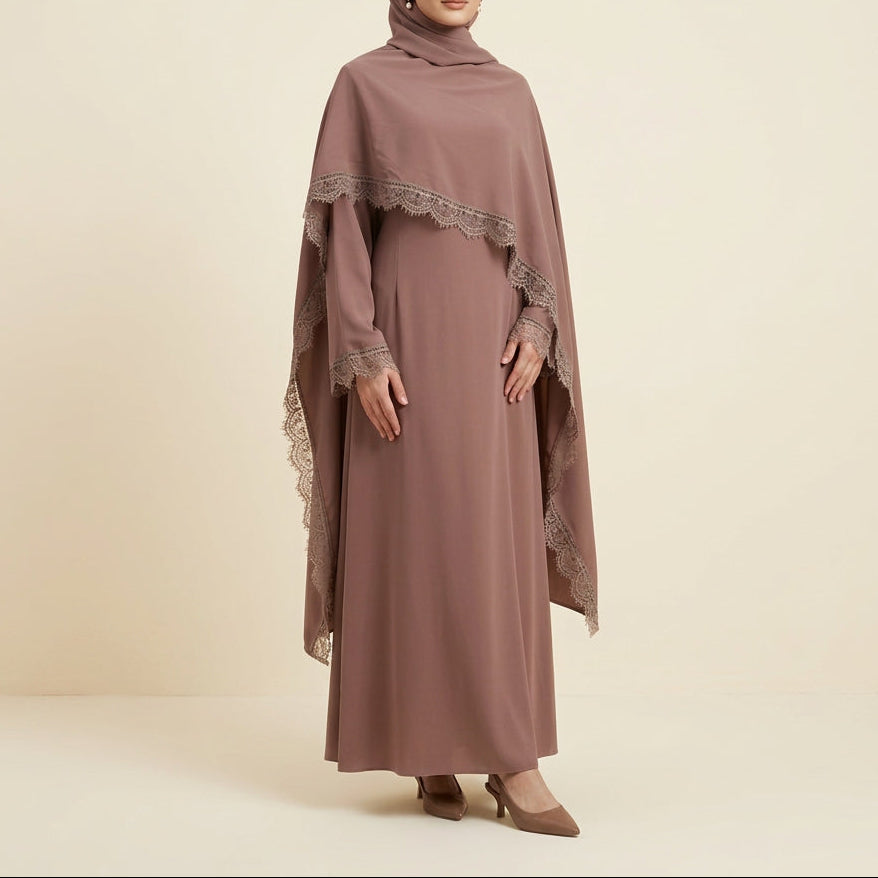 A long-sleeved modest dress in a dusty mauve-brown color, displayed on a mannequin. The dress features draped lace-trimmed shawl overlays on the shoulders and sleeves, set against a white paneled wall background.