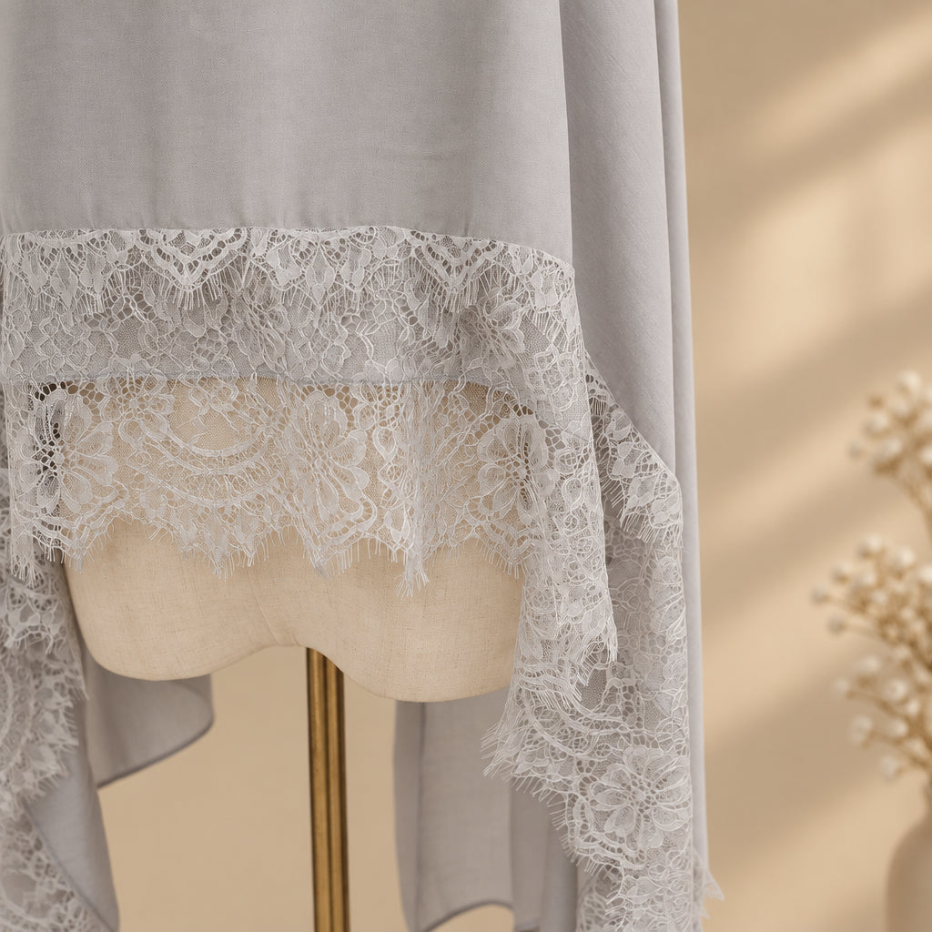 A light gray sheer fabric with a wide white floral lace trim draped over a cream-colored mannequin torso, shown against a plain light gray background.
