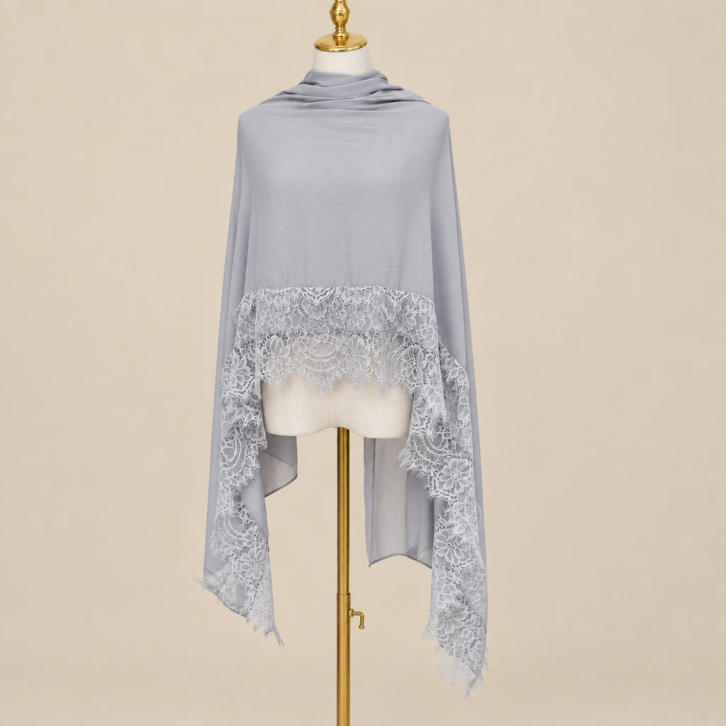 A light gray shawl with a lace hem, draped on a cream-colored dress form mannequin with a gold stand, set against a beige wall 