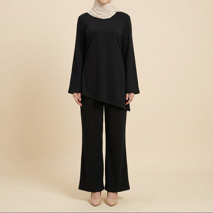 A black two-piece outfit displayed on a dress form, featuring a long-sleeve asymmetrical top and matching wide-leg pants, set against a white paneled wall with a green plant leaf in the corner.