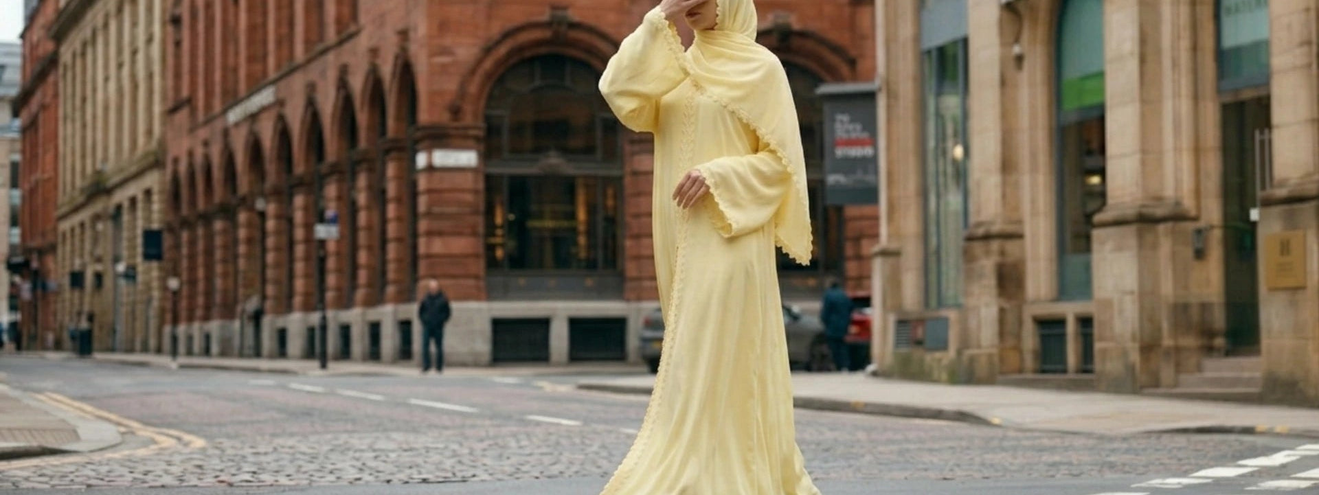 Editorial street style photo of a premium yellow Nida abaya set with matching hijab. The model is standing in a European city setting, showcasing the minimalist design and high-quality fabric of the Spring collection.