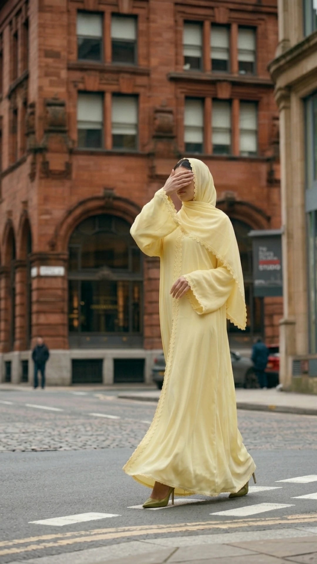 Editorial street style photo of a premium yellow Nida abaya set with matching hijab. The model is standing in a European city setting, showcasing the minimalist design and high-quality fabric of the Spring collection.
